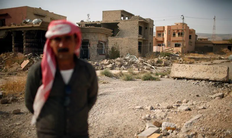 Yazidi man stands in front of destroyed houses in Sinjar