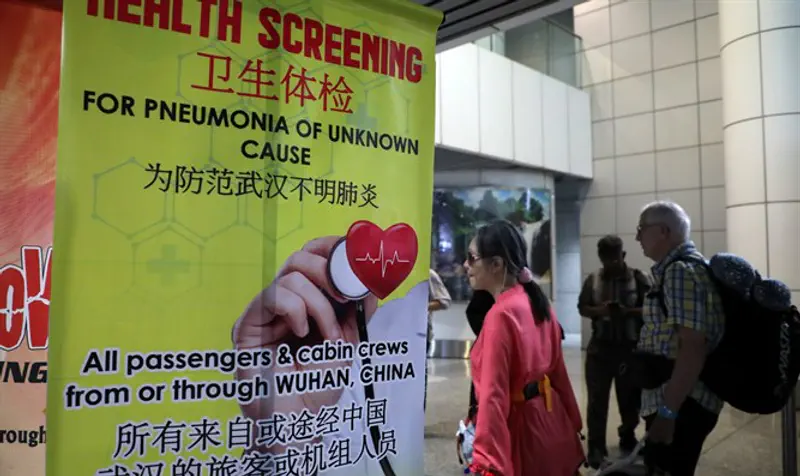 Passengers pass by a banner about Wuhan Pneumonia at thermal screening point