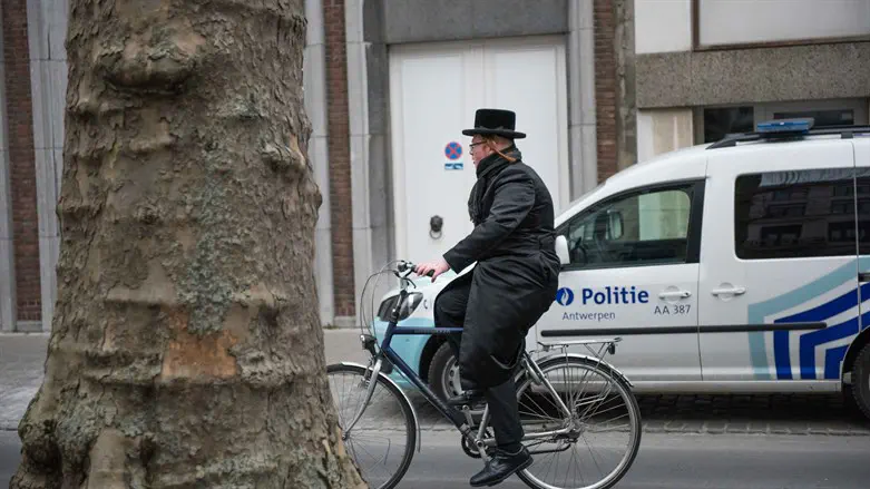 A haredi Jew cycles past a police car in Antwerp, Belgium