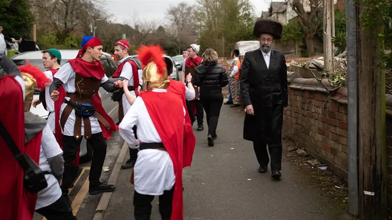 A man wearing haredi attire walks past Jews celebrating Purim in Manchester, UK,