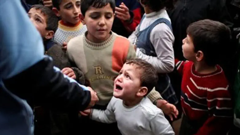 A Syrian child refugee cries in a queue waiting to receive aid in Syria near the Turkish b