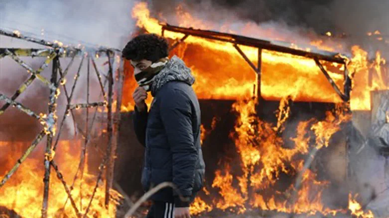Migrant in front of burning hut in Calais "Jungle"