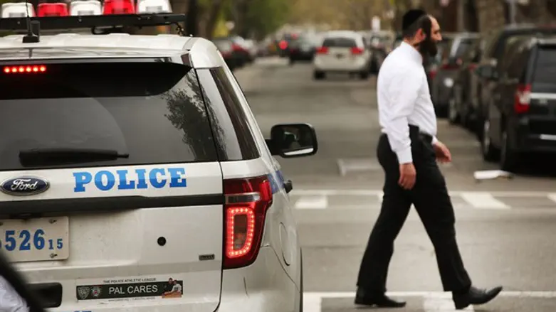 Hasidic man walks by a police car in a Orthodox Jewish neighborhood in Brooklyn