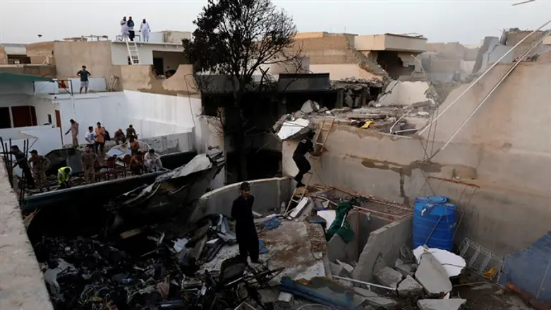 People stand on the roof of a home destroyed after a Pakistani plane crashed int