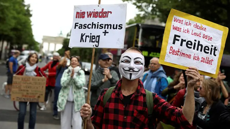 Masked demonstrator holds signs during protest against the COVID-19 restrictions in Berlin