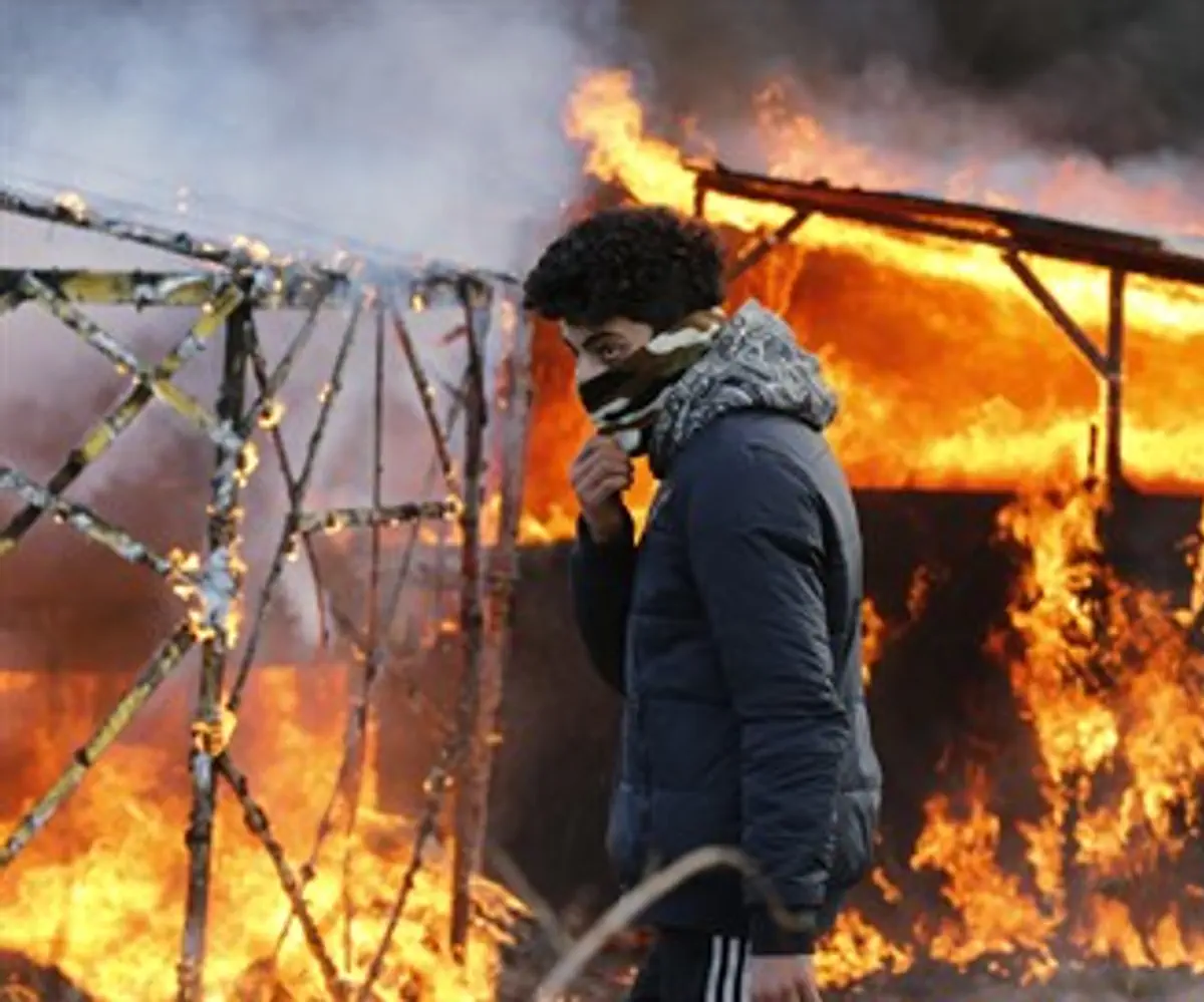 Migrant in front of burning shelter in the Calais 'Jungle'