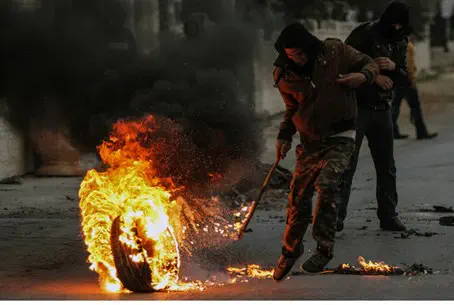 Arab rioter rolls burning tire with a stick