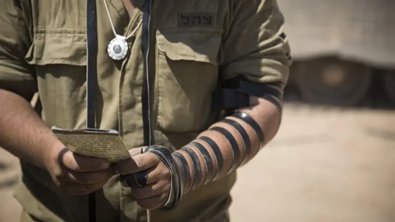 Israeli soldier prays while wearing tefillin at IDF staging area near Gaza